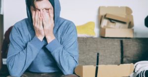 Stressed man surrounded by empty boxes covering his face with his hands