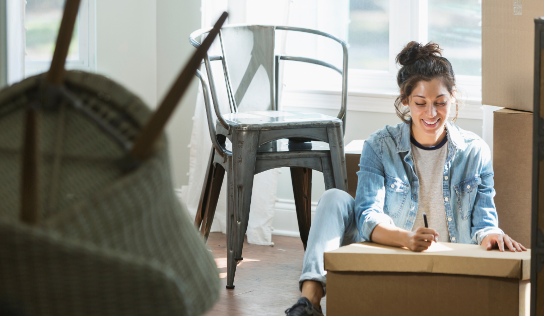 Woman sitting on the surrounded by moving boxes filling out a checklist.