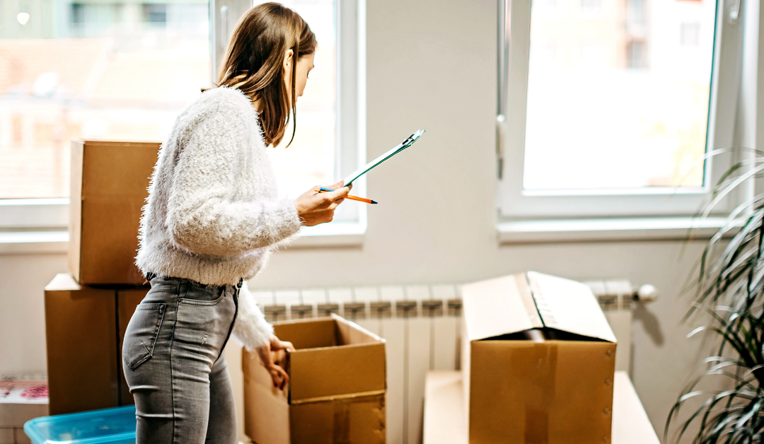 Woman organizing and packing moving boxes with a checklist in hand inside a bright room.