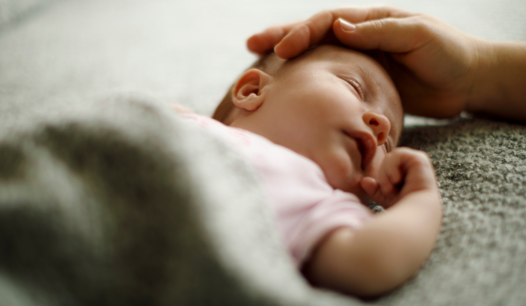 Newborn baby laying under a blanket with their parent caressing their head